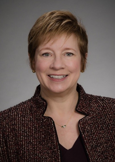 Gail looks at the camera wearing a brown jacket and black shirt.