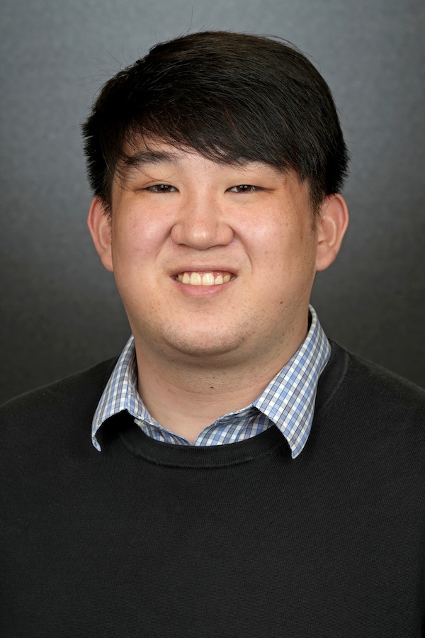 Tyler looks at the camera wearing a black sweater and blue collared shirt.