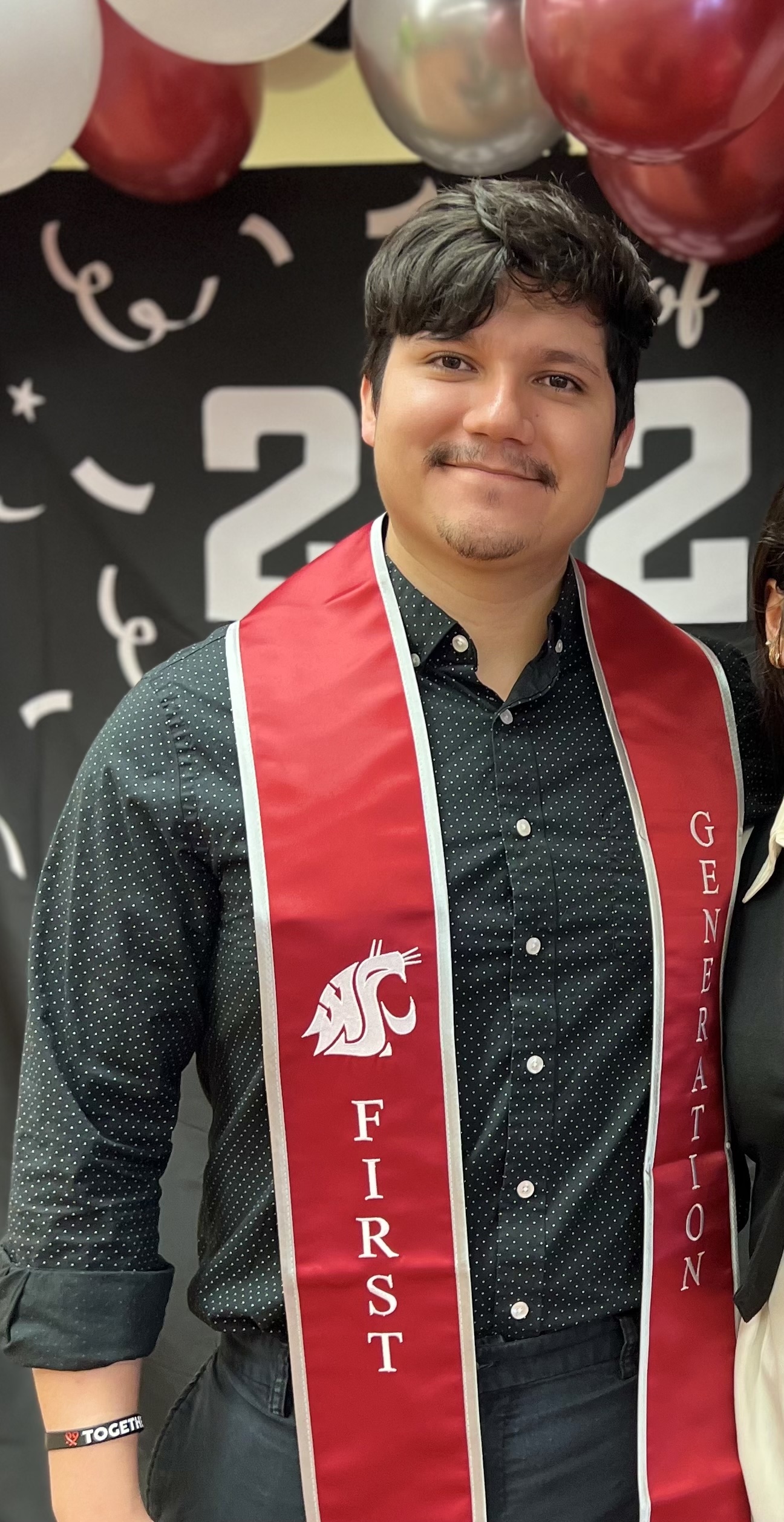 Fernando look at the camera wearing a red graduation sash.