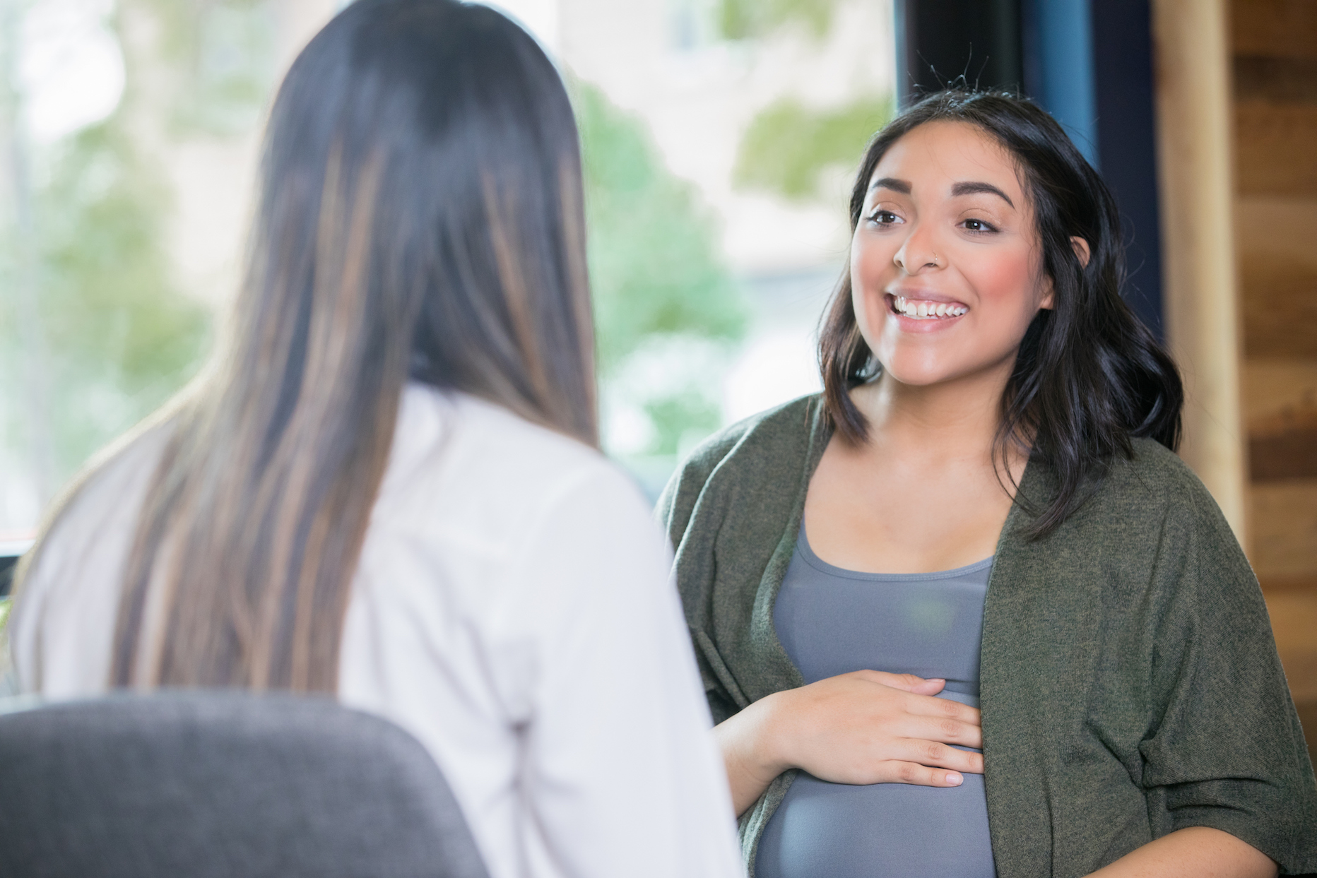 Two women sitting down in a meeting and one is pregnant