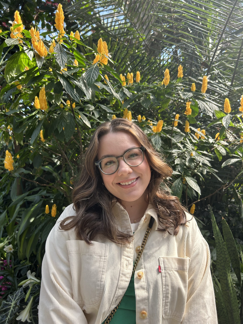 Oliwia looks at the camera in front of a flowering plant.