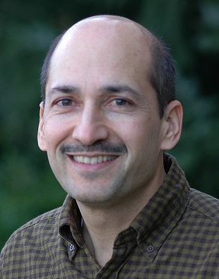 Raj looks at the camera wearing a brown collared shirt.