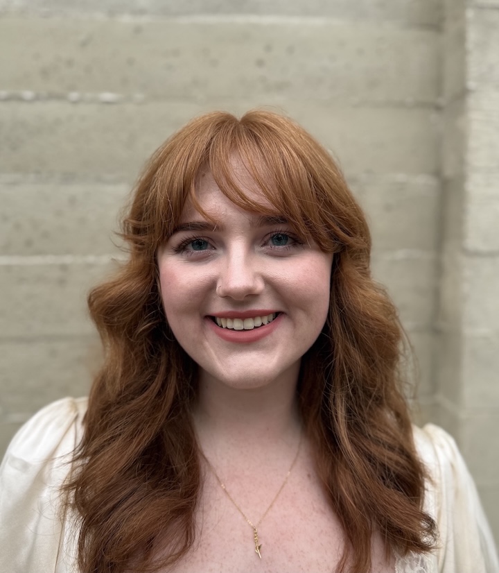 Kiana smiles at the camera standing in front of a white brick wall.