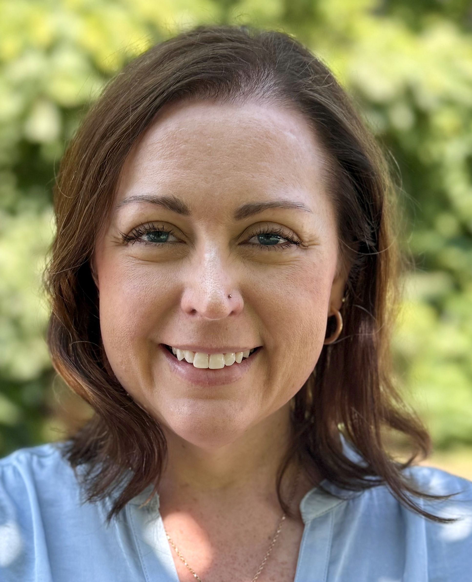 Jill smiles at the camera wearing a blue button up shirt.