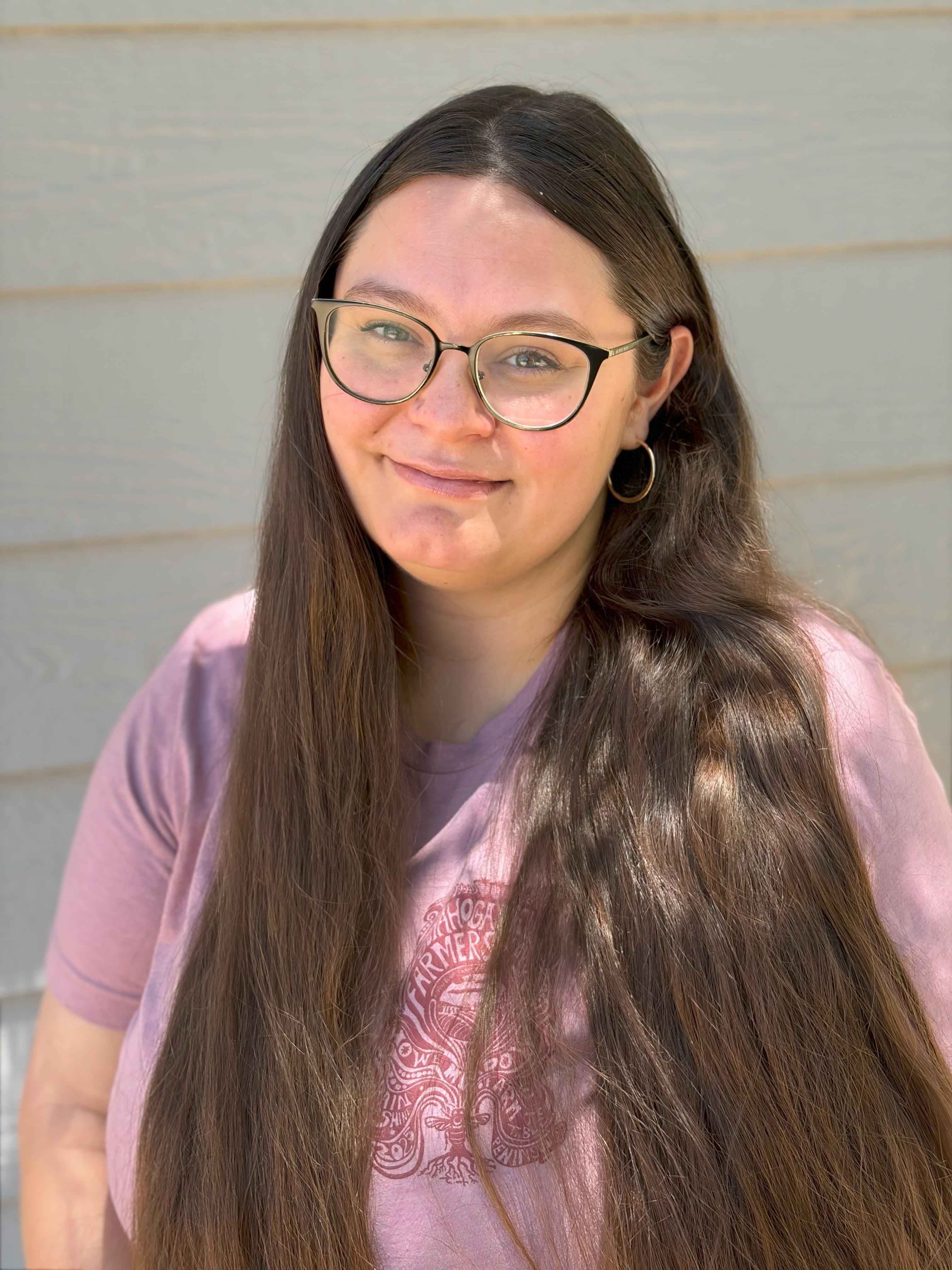 Laurie Ferrato smiles at the camera wearing a pink shirt and glasses.
