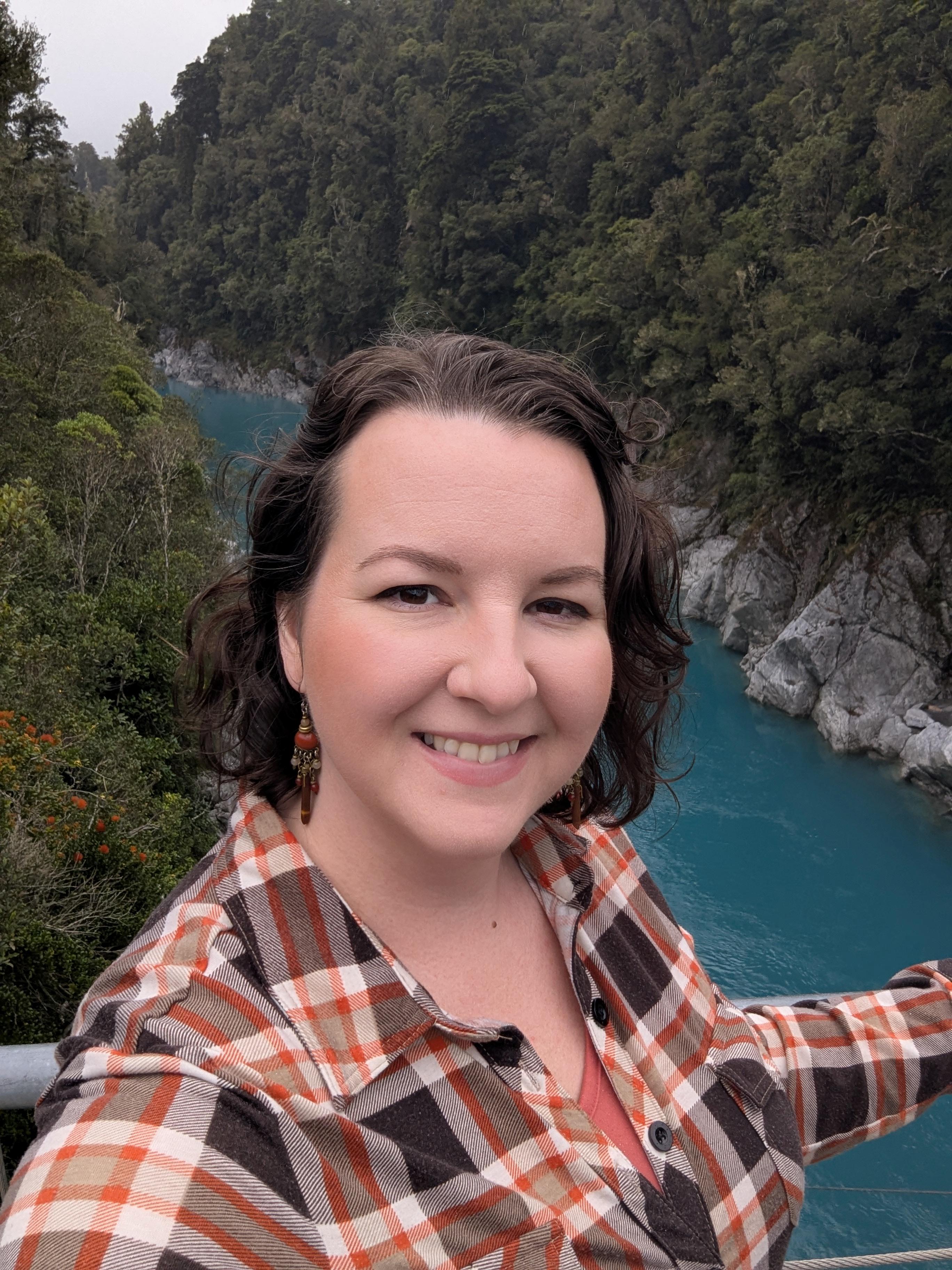 Misa looks at the camera with a river and trees behind her.
