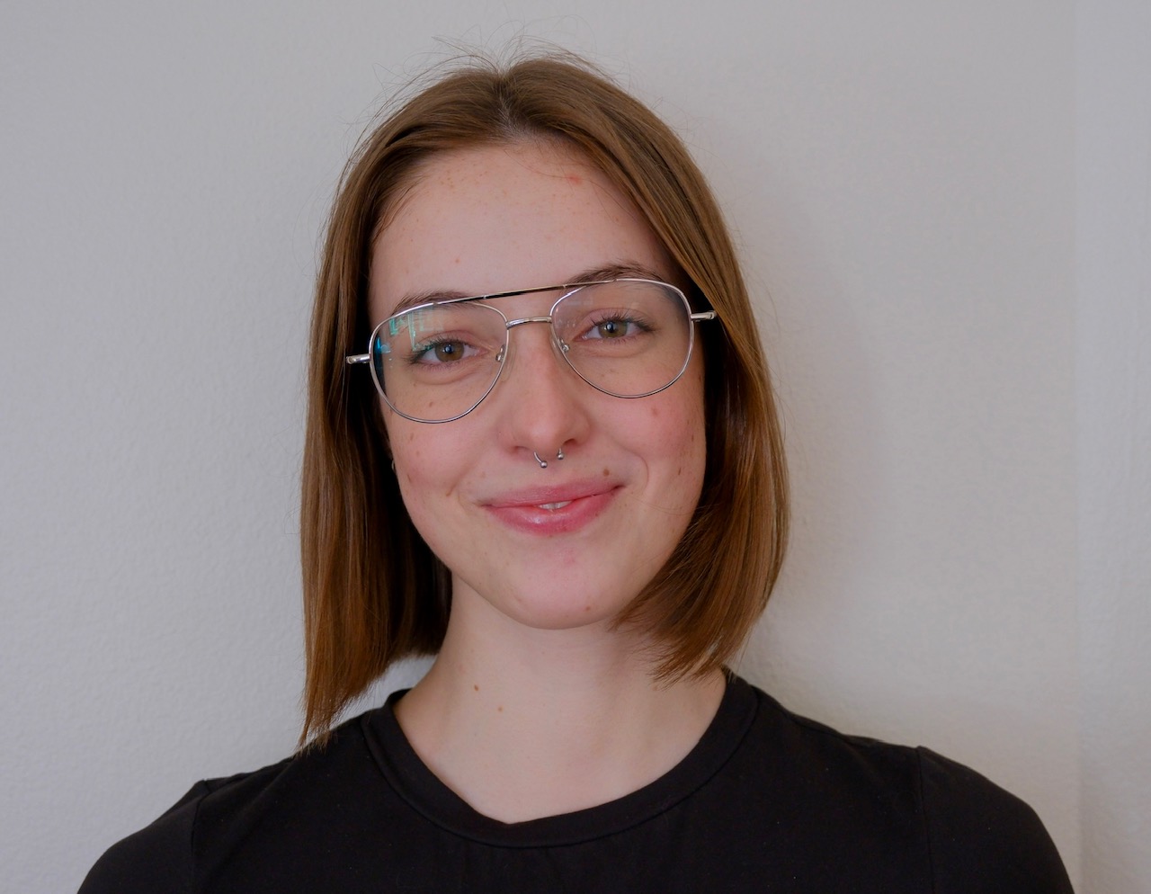 Zoe smiles at the camera wearing a black shirt and glasses.